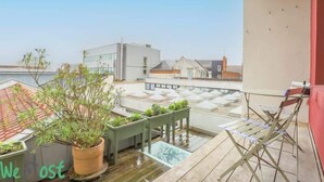 Eine Dachterrasse mit Blumentöpfen, einem Klapptisch und Stühlen.