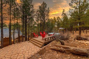 Une terrasse en bois avec des chaises rouges et une table, entourée d’arbres et bordée d’un chemin en pierre.