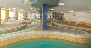 En indendørs swimmingpool med flere baner, liggestole og en central søjle.