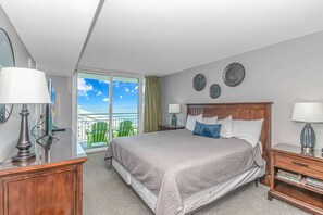 Et hotelværelse med seng, to sengeborde, et vindue med udsigt til stranden og en balkon.