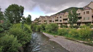 Eine Reihe moderner, mehrstöckiger Gebäude mit Balkonen, ein Fluss im Vordergrund und eine hügelige Landschaft im Hintergrund.