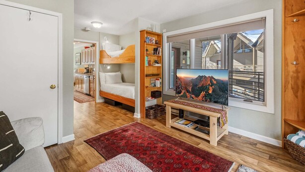 Ein gemütlicher Raum mit Etagenbett, Bücherregal, Fernseher und einem großen Fenster mit Blick auf die Berge.