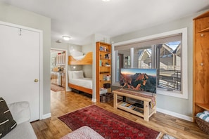 Ein gemütlicher Raum mit Etagenbett, Bücherregal, Fernseher und einem großen Fenster mit Blick auf die Berge.