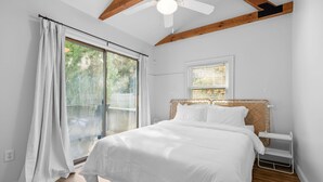 Un dormitorio con una cama grande, ventilador de techo, ventana con persianas y vistas al exterior.