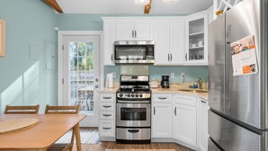Una cocina moderna con armarios blancos, electrodomésticos de acero inoxidable y una zona de comedor con una mesa y sillas de madera.