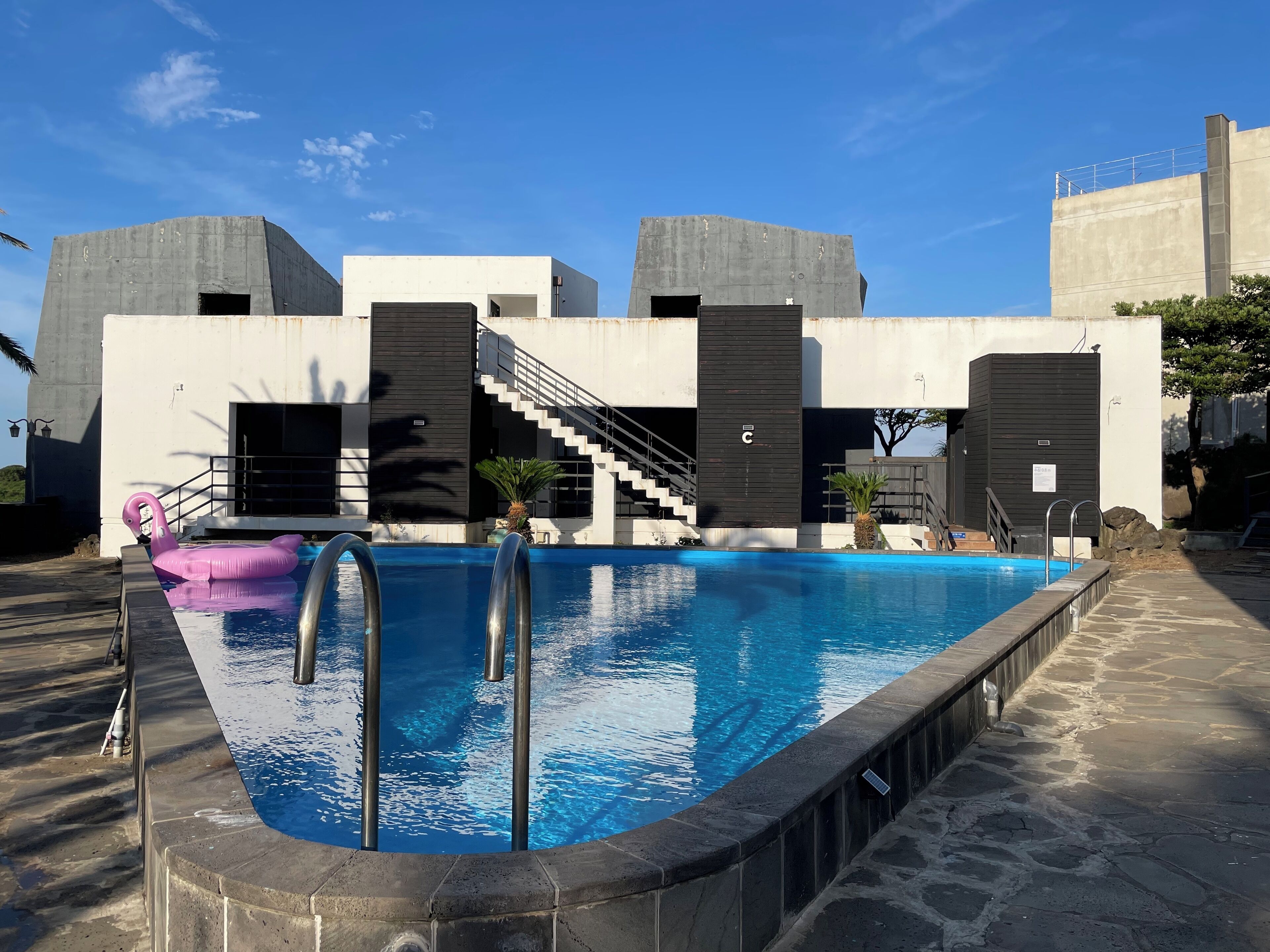 A modern pool area with a clear blue pool, a pink float, and a staircase leading to a black and white building.