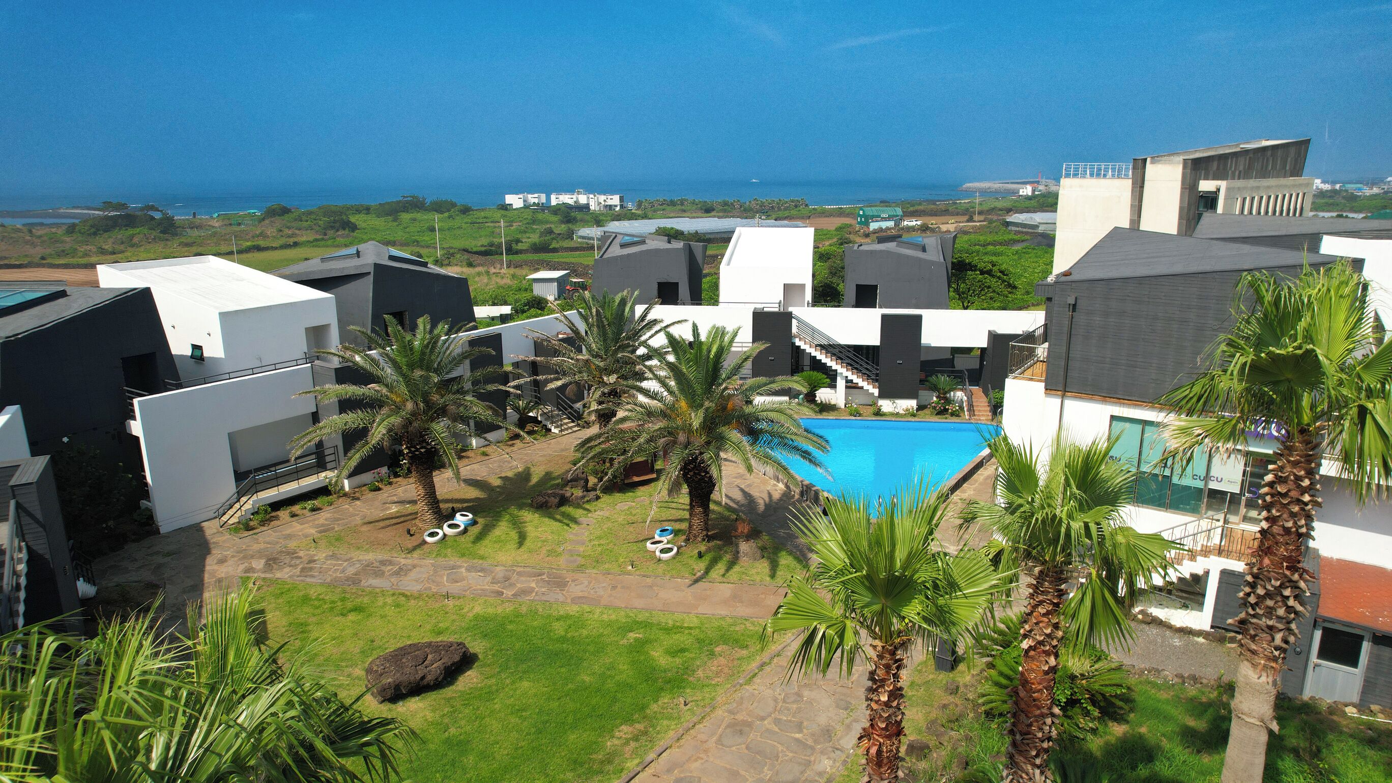 A modern resort with a swimming pool surrounded by palm trees and a view of the ocean.