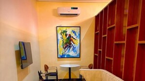 A modern living room with a beige sofa, a small round table, and a colorful abstract painting on the wall. - Kim Royal Hotel and Suites (Asaba)