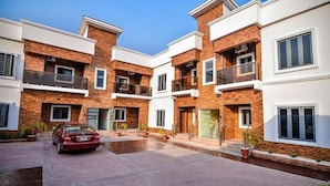 A modern multi-story residential building with balconies, a driveway, and potted plants. - Kim Royal Hotel and Suites (Asaba)