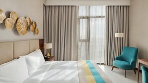 A hotel room with a bed, a chair, a lamp, and a window with curtains. - Standard Room Near Maktoum Airport By E R (Dubai)