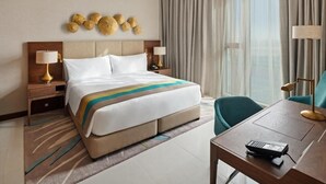 A hotel room with a large bed, two bedside tables with lamps, a desk with a telephone, and a view of the outdoors through sheer curtains. - Standard Room Near Maktoum Airport By E R (Dubai)
