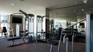 A gym with exercise equipment, a mirror, and a television on the wall. - Standard Room Near Maktoum Airport By E R (Dubai)