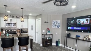 A modern kitchen with white cabinets, a stainless steel oven, and a dining area with two bar stools. - Luxe King Suite Bliss Getaway Condo Near Disney  (Kissimmee)