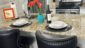 A modern kitchen with granite countertops, a built-in oven, and a dining area with two black leather chairs. - Luxe King Suite Bliss Getaway Condo Near Disney  (Kissimmee)