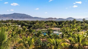 Paisatge amb palmeres, una piscina i muntanyes al fons.