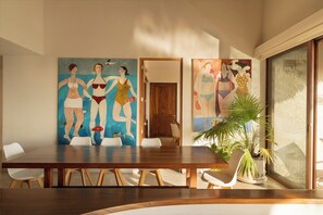 Een eethoek met een houten tafel en stoelen, een groot schilderij aan de muur en een kamerplant.