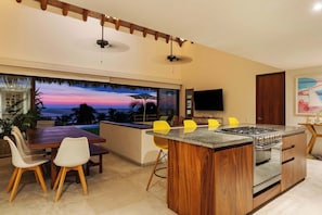 A modern kitchen with a large island, dining area with chairs, and a view of the ocean. - Zihuatanejo 4BR • Artful Beach Villa + Pool (Zihuatanejo)