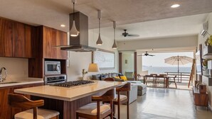 A modern kitchen with a central island, bar stools, and a view to the outside.
