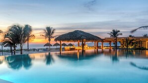A poolside area with a sunset view, palm trees, and a thatched-roof structure. - Bright 2BR Villa I Sea Views + Open Kitchen (Zihuatanejo)