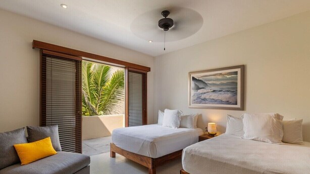 A hotel room with two beds, a sofa, and a ceiling fan.