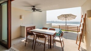 A balcony with a dining table and chairs, a ceiling fan, and a beach view.