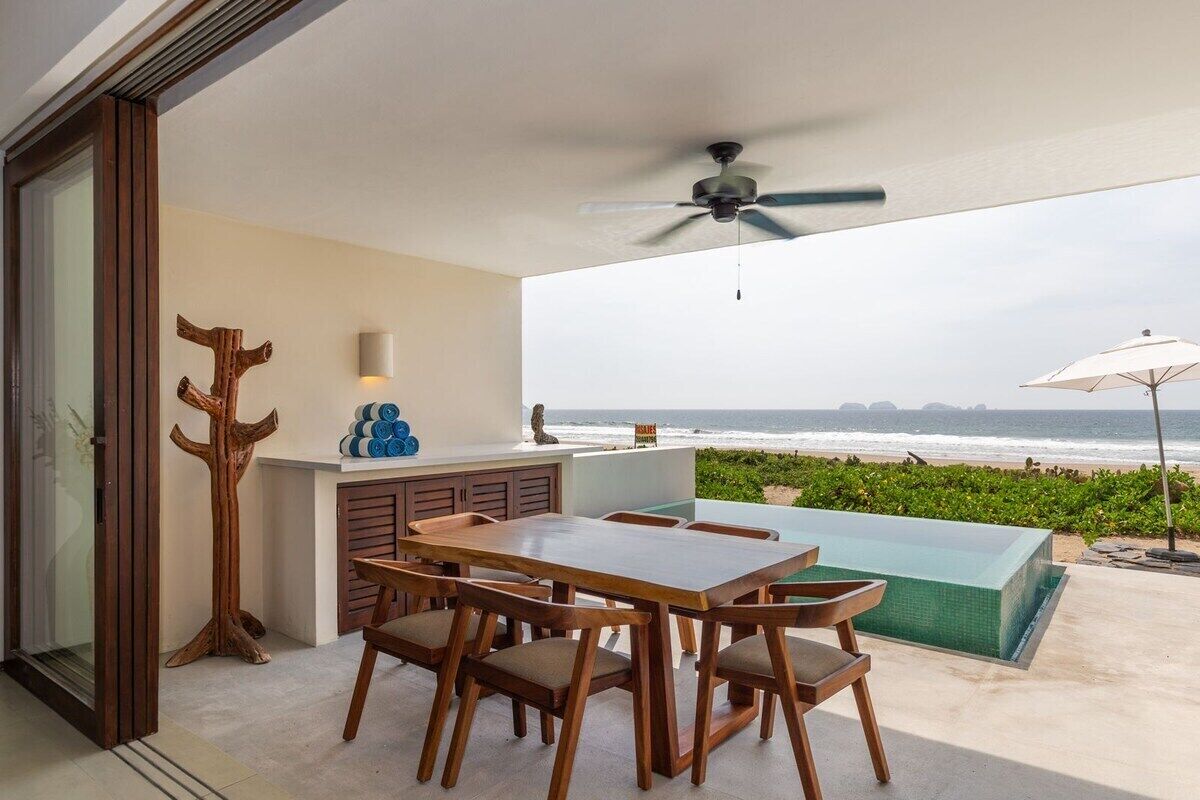Ein Balkon mit Blick auf den Ozean, ein Holztisch und Stühle, ein Deckenventilator und ein kleiner Pool.