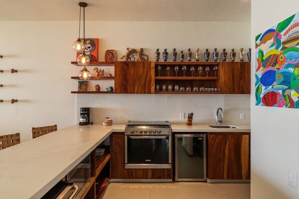 A modern kitchen with wooden cabinets, a built-in oven, a dishwasher, and a dining area with a long table.