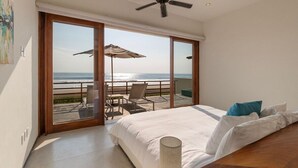 A bedroom with a large bed, a ceiling fan, and a view of the beach through a sliding glass door. - Modern 2BR Villa  w/ Sea Views + Breezy Terrace (Zihuatanejo)