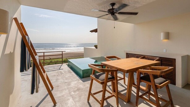 A modern outdoor dining area with a view of the ocean, a ceiling fan, and a pool. - Modern 2BR Villa  w/ Sea Views + Breezy Terrace (Zihuatanejo)