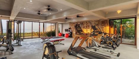 A gym with various exercise equipment, large windows, and a stone wall.