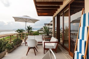 A balcony with a view of the beach, white cushioned chairs, a large umbrella, and potted plants. - 2BR Beachfront Villa + Pool, Style & Sea Views (Zihuatanejo)
