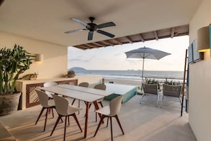 An outdoor patio with a dining table, chairs, a ceiling fan, a large umbrella, and a view of the ocean. - 2BR Beachfront Villa + Pool, Style & Sea Views (Zihuatanejo)
