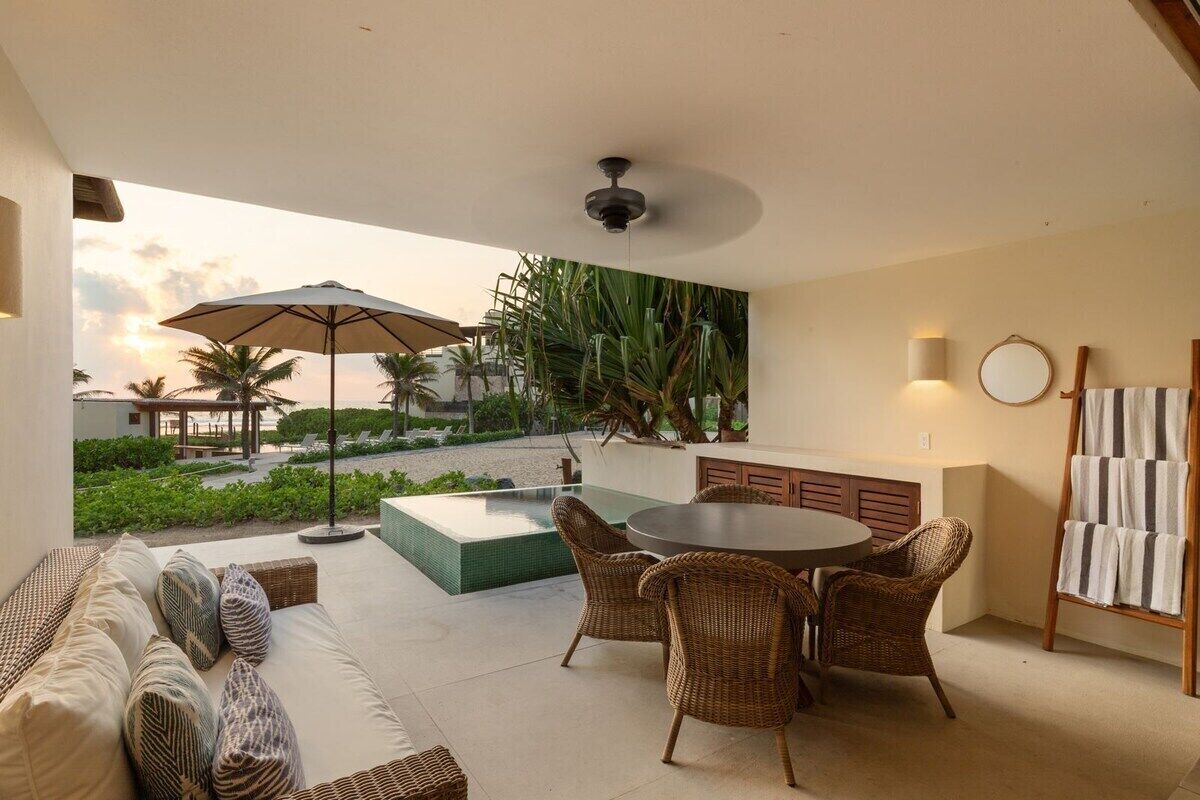 A modern outdoor seating area with a round table and wicker chairs, a sofa with patterned cushions, and a large umbrella.