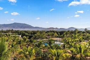 A landscape with palm trees, a pool, and mountains in the background.