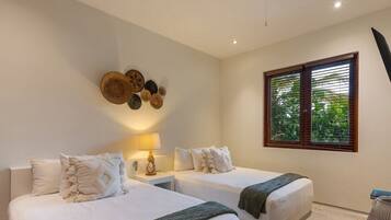 Habitación de hotel con dos camas, un adorno en la pared, una ventana con persianas y una mesita de noche con lámpara.