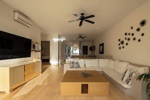A modern living room with a flat-screen TV, wooden coffee table, white sofa, ceiling fans, and decorative wall art.