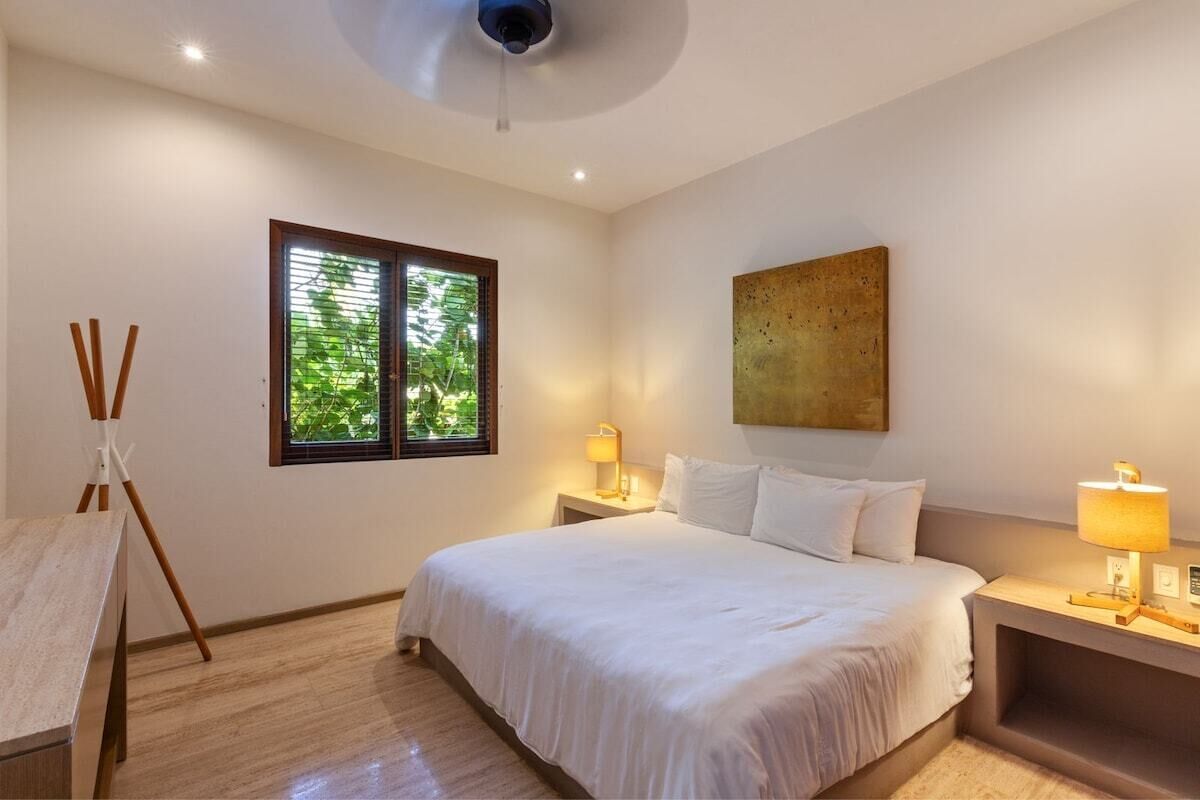 Une chambre d’hôtel avec un lit, des lampes de chevet, une fenêtre avec des stores et un ventilateur de plafond.