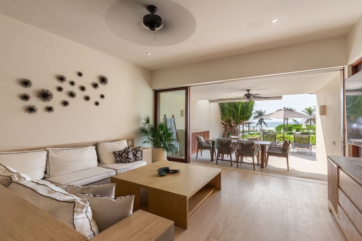 Un salon moderne avec un canapé, une table basse et un coin repas avec des chaises. Une grande fenêtre offre une vue sur l’extérieur.