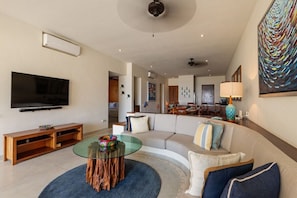A modern living room with a flat-screen TV, a glass coffee table, and a sofa.