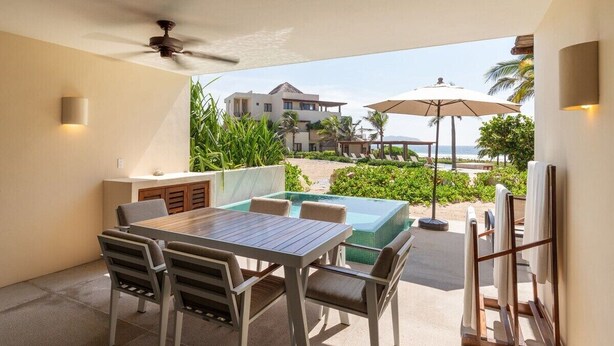 Een terras met tafel en stoelen, een klein zwembad en uitzicht op strand en zee.