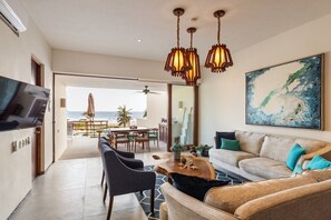 A modern living room with a sofa, chairs, a coffee table, and a TV. There is a balcony with a view of the ocean. - Elegant 2BR Villa I Ocean View + Artful Style (Zihuatanejo)