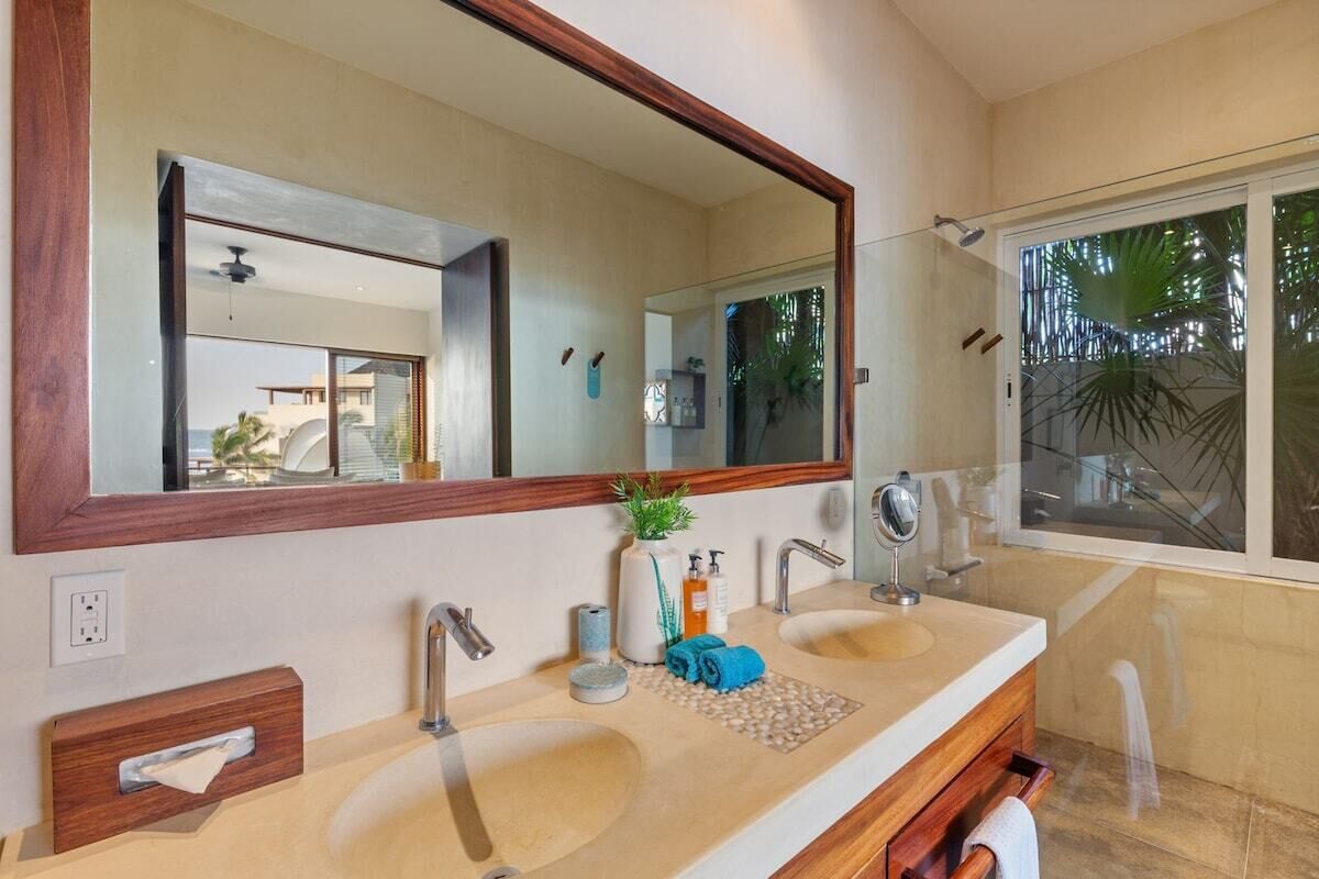 A bathroom with two sinks, a large mirror, and a window with a view of palm trees.