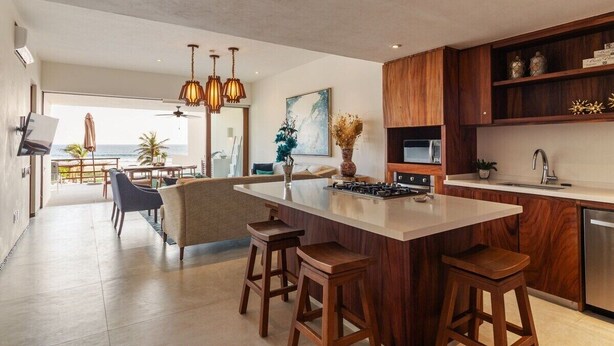 A modern kitchen with a central island, bar stools, wooden cabinetry, and a view to the outside. - Elegant 2BR Villa I Ocean View + Artful Style (Zihuatanejo)