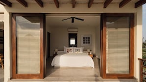 A bedroom with a bed centered in a room with a ceiling fan, a window with blinds, and a door leading to another area. - 2BR Ocean View Apt | Exclusive Zihua Stay (Zihuatanejo)