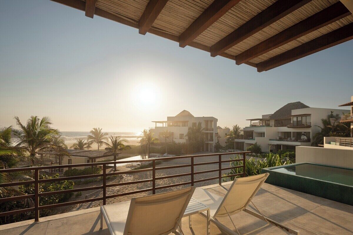 Un balcon avec vue sur la plage et l’océan, une piscine et des chaises longues.