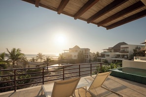 A balcony with a view of the beach and ocean, a pool, and lounge chairs.
