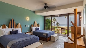 Un dormitorio con dos camas, un balcón con vistas a la playa y un escritorio de madera.