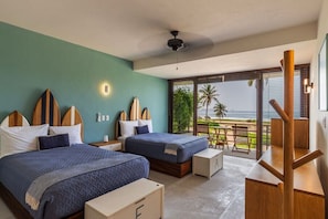 Quarto com duas camas, varanda com vista para a praia e escrivaninha de madeira.