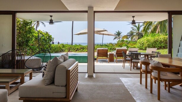 Un interior moderno con sofá, mesa de comedor y sillas, piscina y vistas al océano.