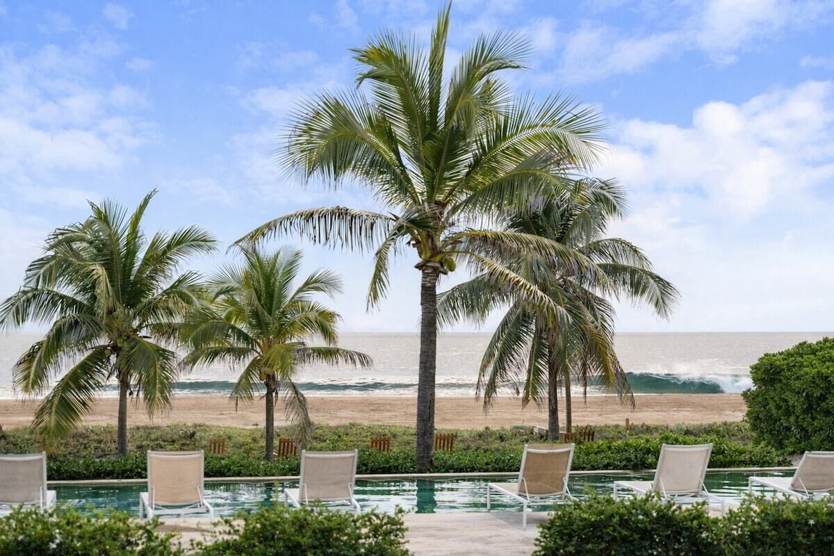Ein Poolbereich mit Liegestühlen und Palmen mit Blick auf einen Strand.
